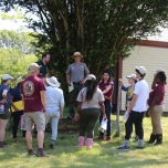 Debriefing the Inventory Team: Bill Burke (center, with brimmed hat) explains the history of the site to the group in the shade of a large tree-of-heaven. Behind him is the north façade of the main house.